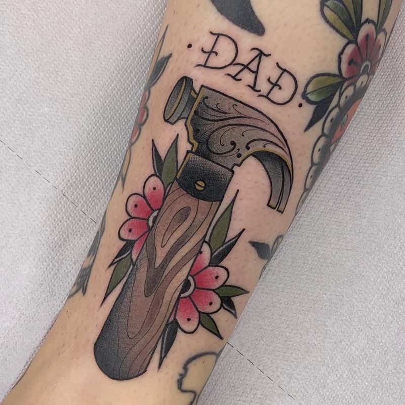 Hammer-Tattoo mit Schriftzug „Dad“ und Blumen am Unterarm